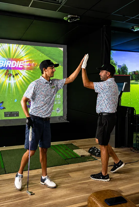 Two golfers high-fiving inside a TeedUp simulator bay